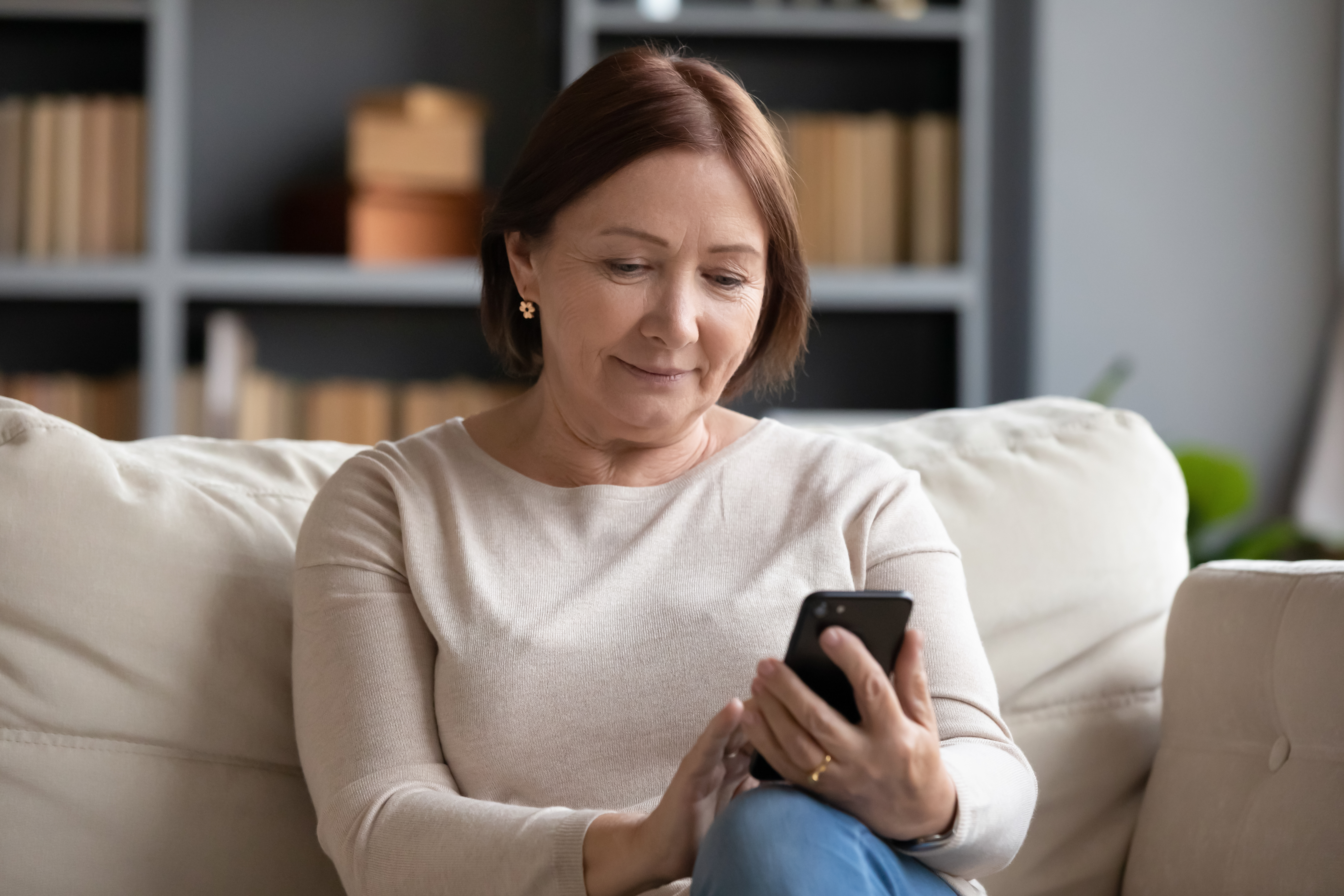 Photograph of a woman on a couch looking at a smartphone.