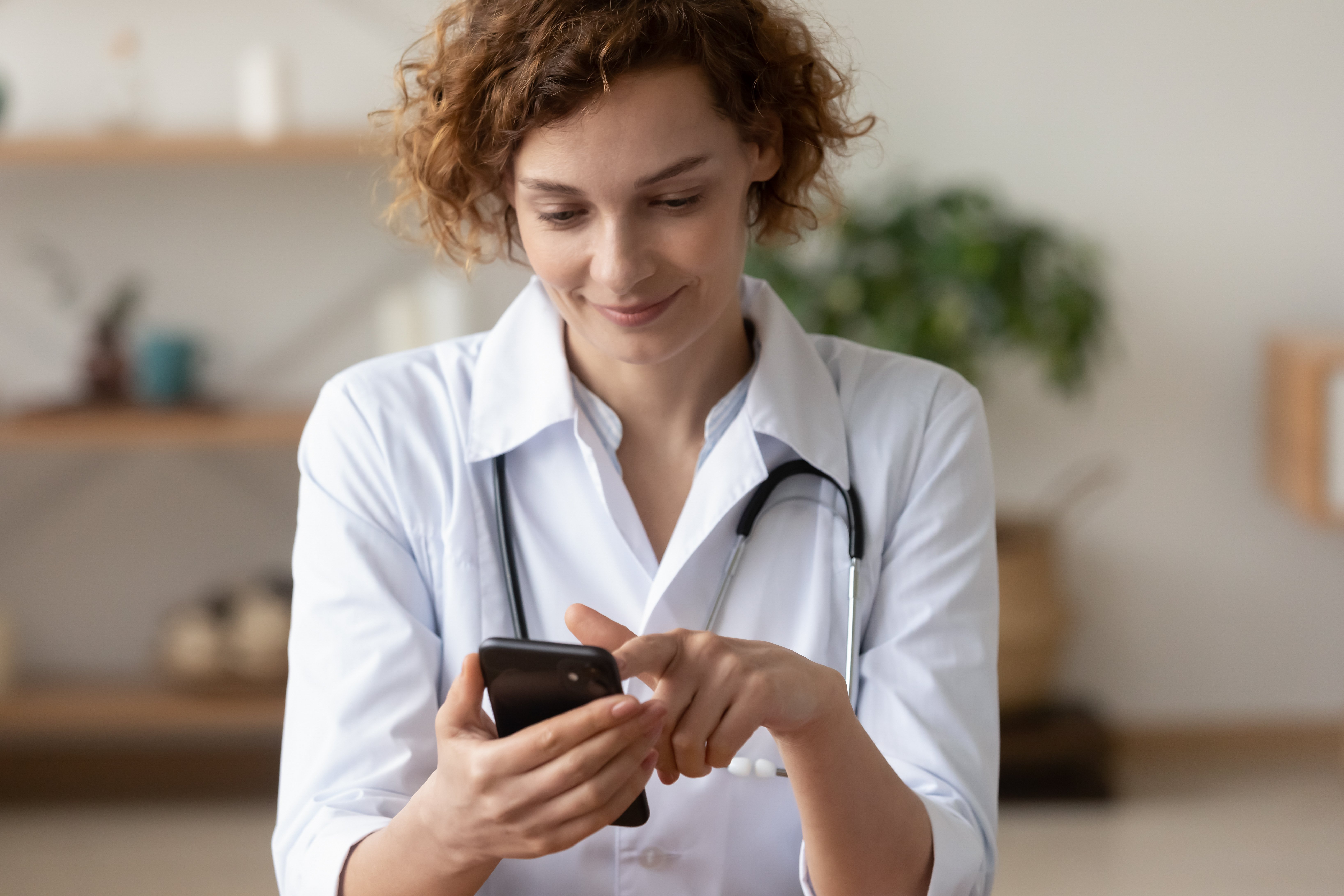A doctor in a white coat with a stethoscope swipes on her phone.